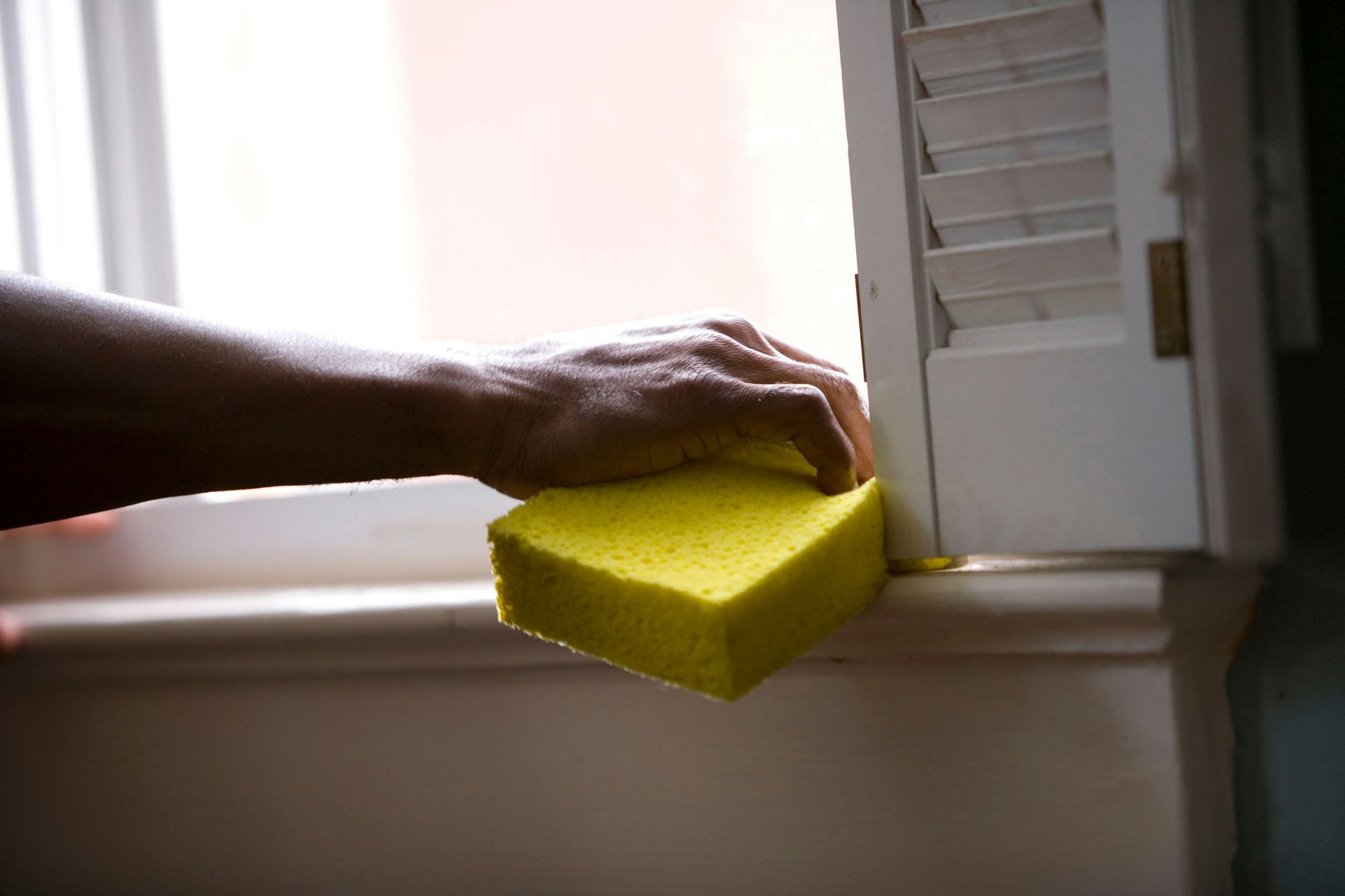Hand with sponge cleaning the edge of a window