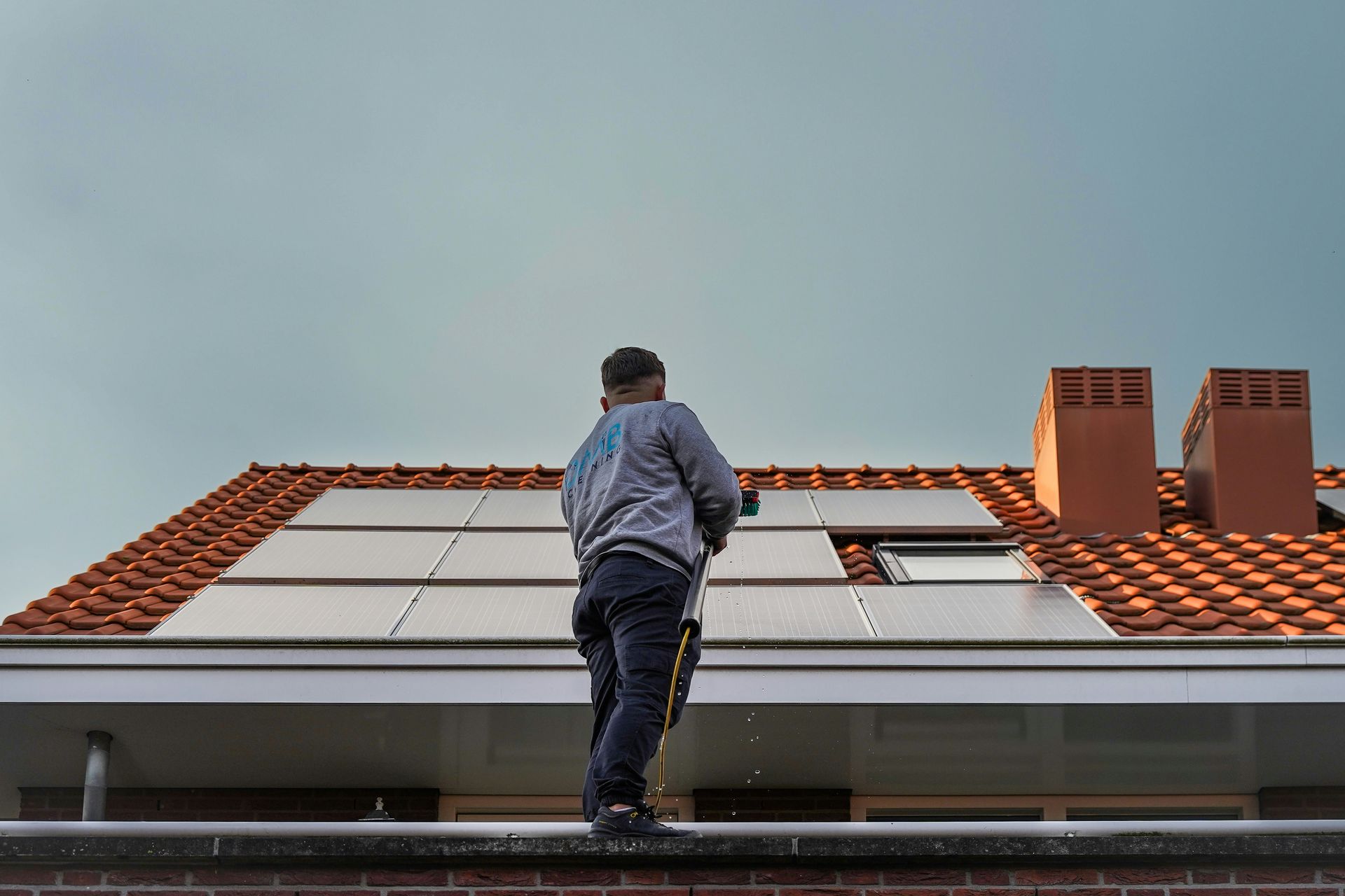Man on a house roof top cleaning solar panels