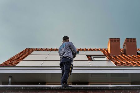 Man on a house roof top cleaning solar panels