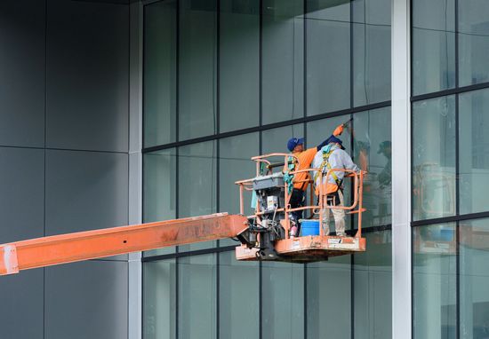 Two workers in a cherry picker cleaning  an office window panel