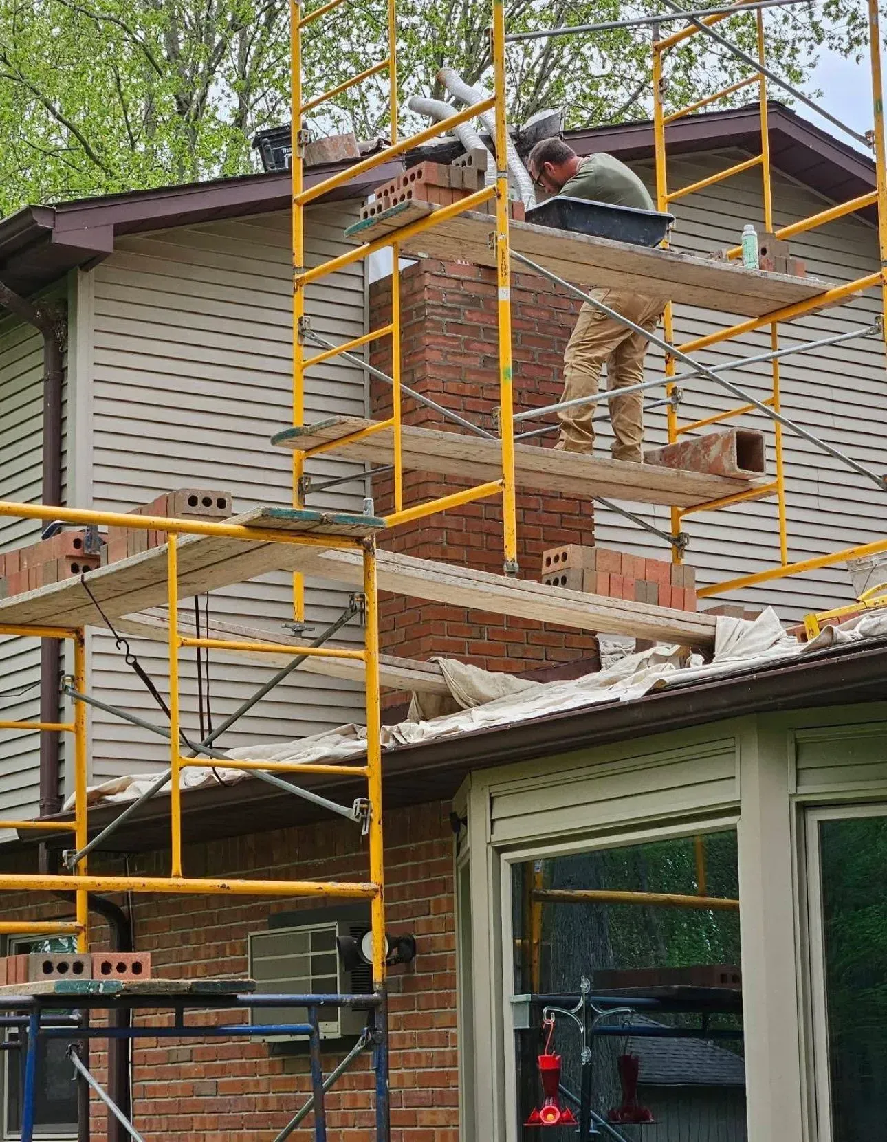 Person on scaffolding repairing a brick chimney on a house.