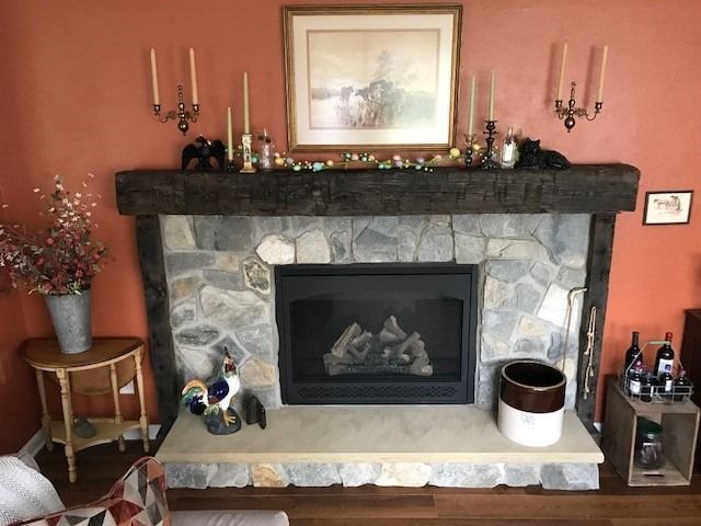 Fireplace with stone facade, dark wood mantel, and orange wall. Decorated with candles, art, and decorative items.