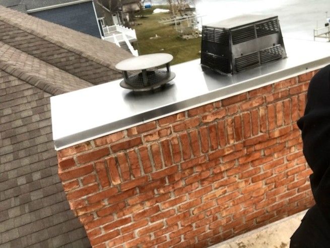 Brick chimney with stainless steel cap, vent, and chimney topper on a roof.