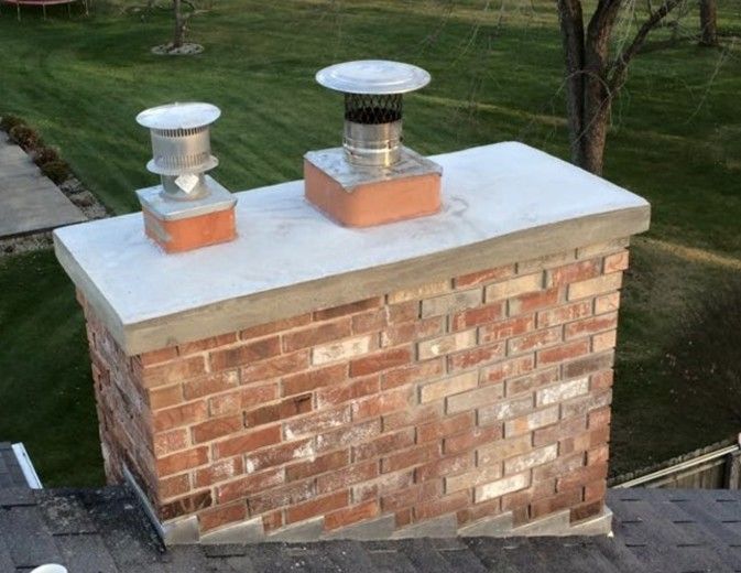 Brick chimney with two metal chimney caps on a white concrete top.