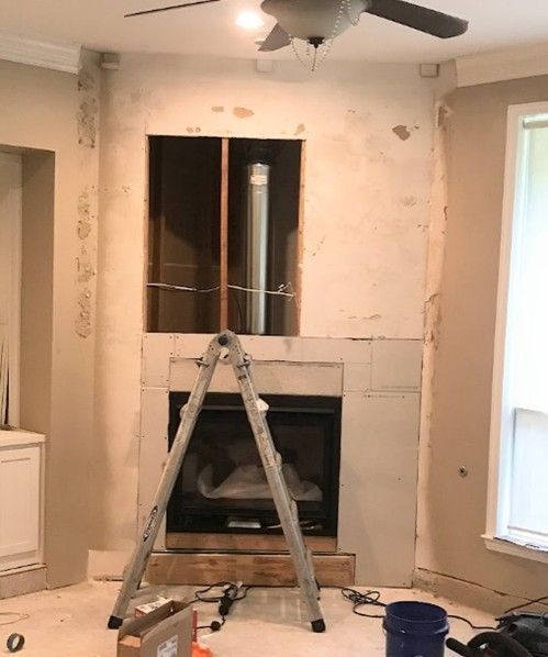 Fireplace under construction, with exposed framing and a ladder. The surrounding walls are beige.