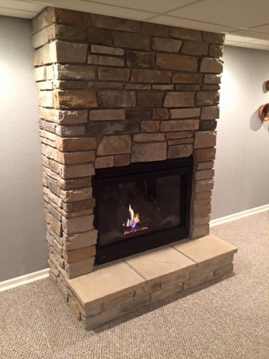Fireplace with stone facade, flames visible inside, set in a room with neutral walls and carpet.
