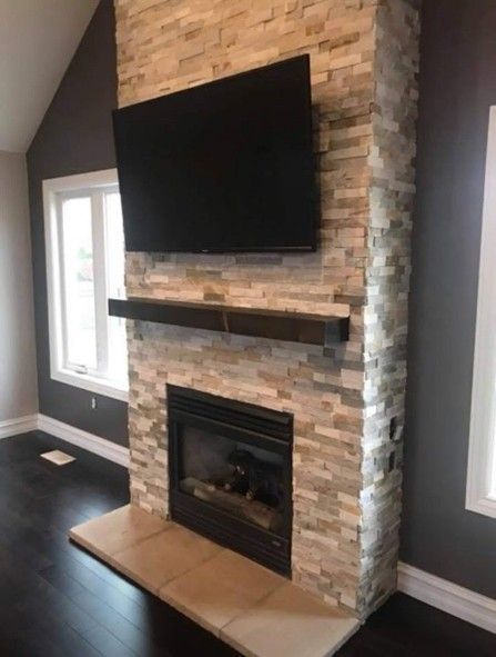 Fireplace with a stone facade, built-in TV, and dark wood mantel against a dark grey wall.