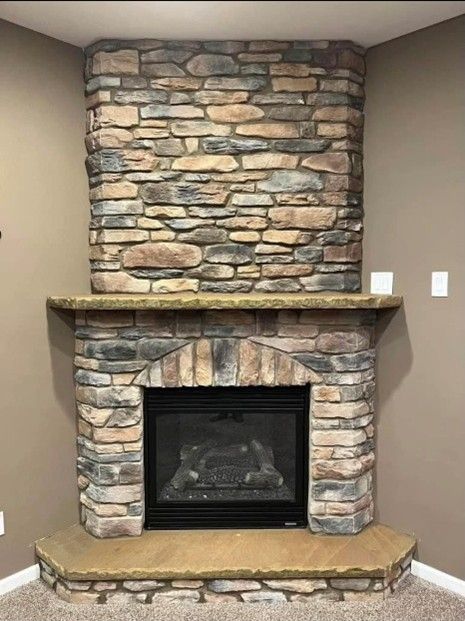 Stone fireplace in a corner. Beige and gray stone with a black firebox. Light brown walls and hearth.