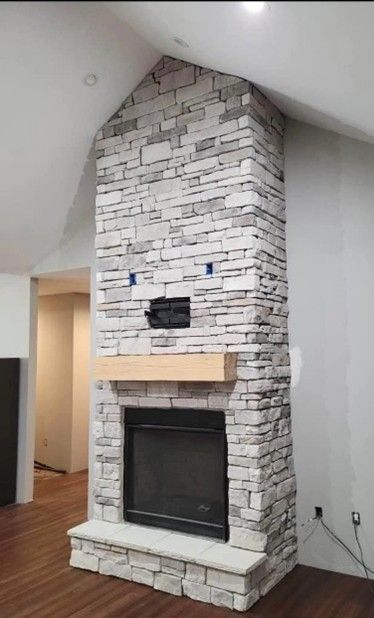 Stone fireplace in a room with hardwood floors and drywall walls, featuring a wooden mantel and recessed firebox.