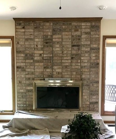 Brick fireplace with wooden trim, flanked by windows. Covered furniture in front.