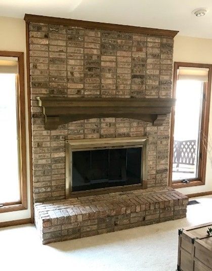Brick fireplace with wooden mantel and trim, flanked by windows.