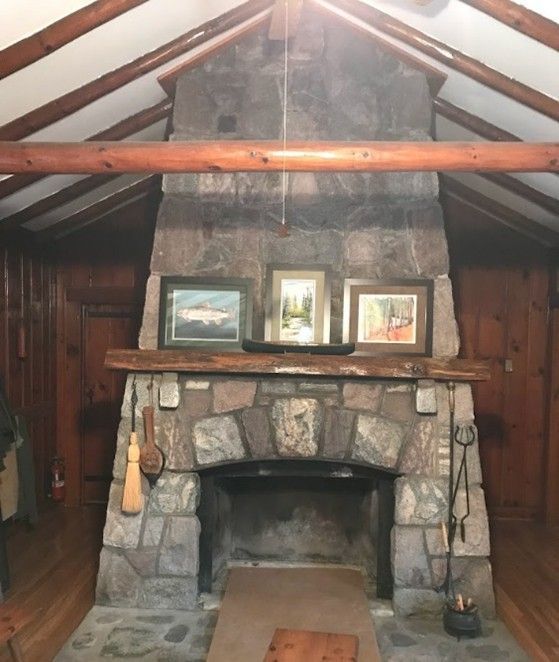 Stone fireplace in a cabin; framed art above mantel, wooden beams overhead.
