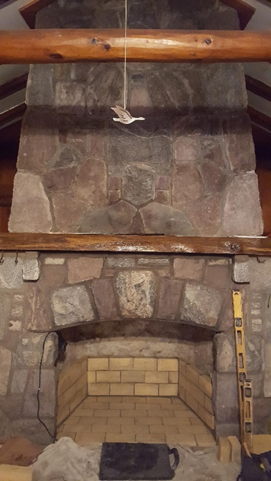 Stone fireplace with a brick firebox, wooden mantel, and carved bird hanging above.