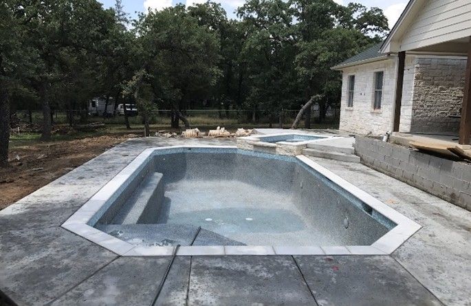 Empty rectangular pool with steps, concrete patio, jacuzzi, and a house.