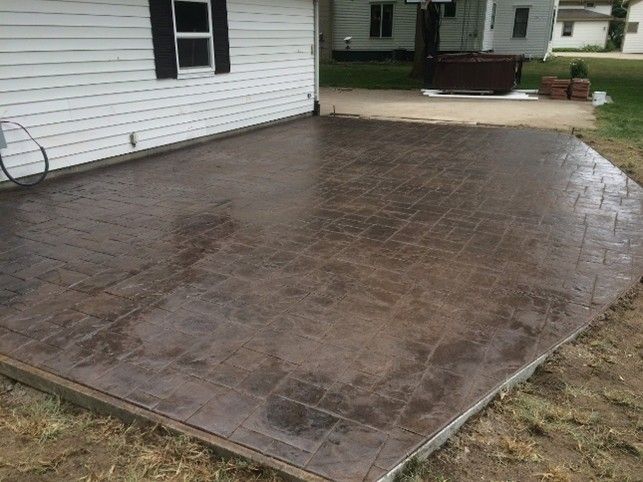 Brown stamped concrete patio next to a white house with a black shutter.