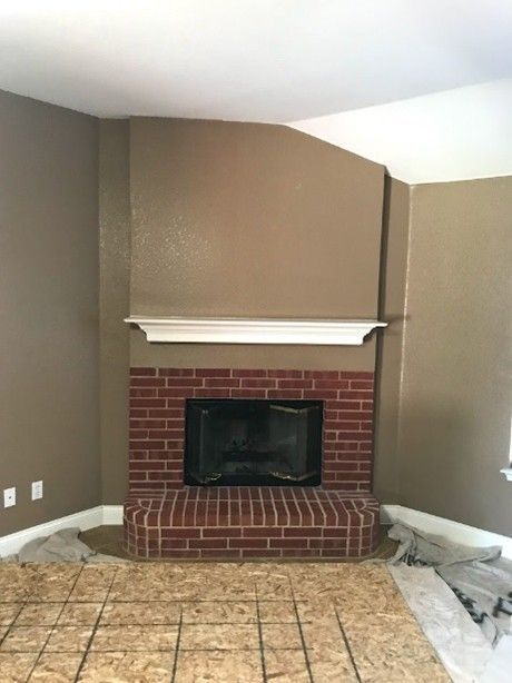 Brick fireplace with a white mantel, brown walls, and exposed subfloor.