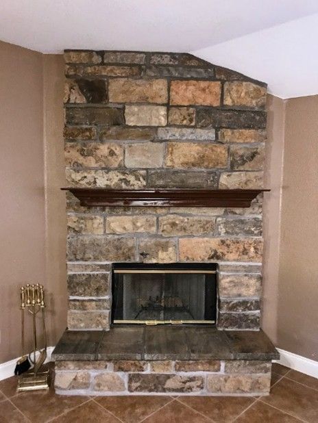Stone fireplace with brown mantel in a room with beige walls.