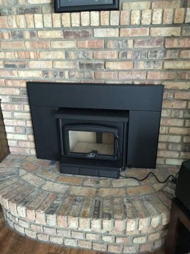 A black stove is set into a brick fireplace. The fireplace includes a brick hearth and a black surround.