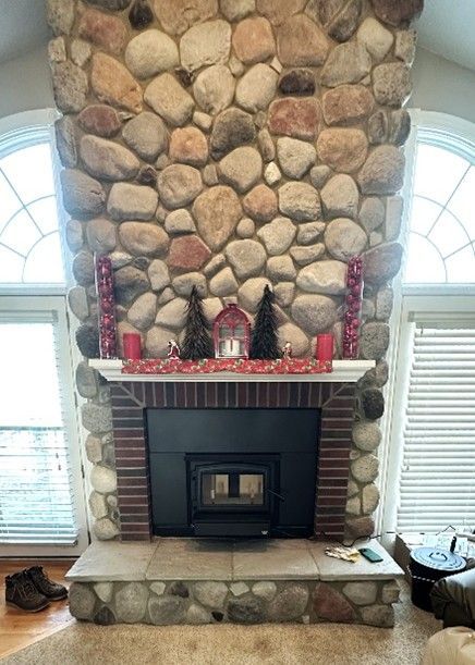 Stone fireplace with a black insert, brick surround, and mantle with decorations between two arched windows.