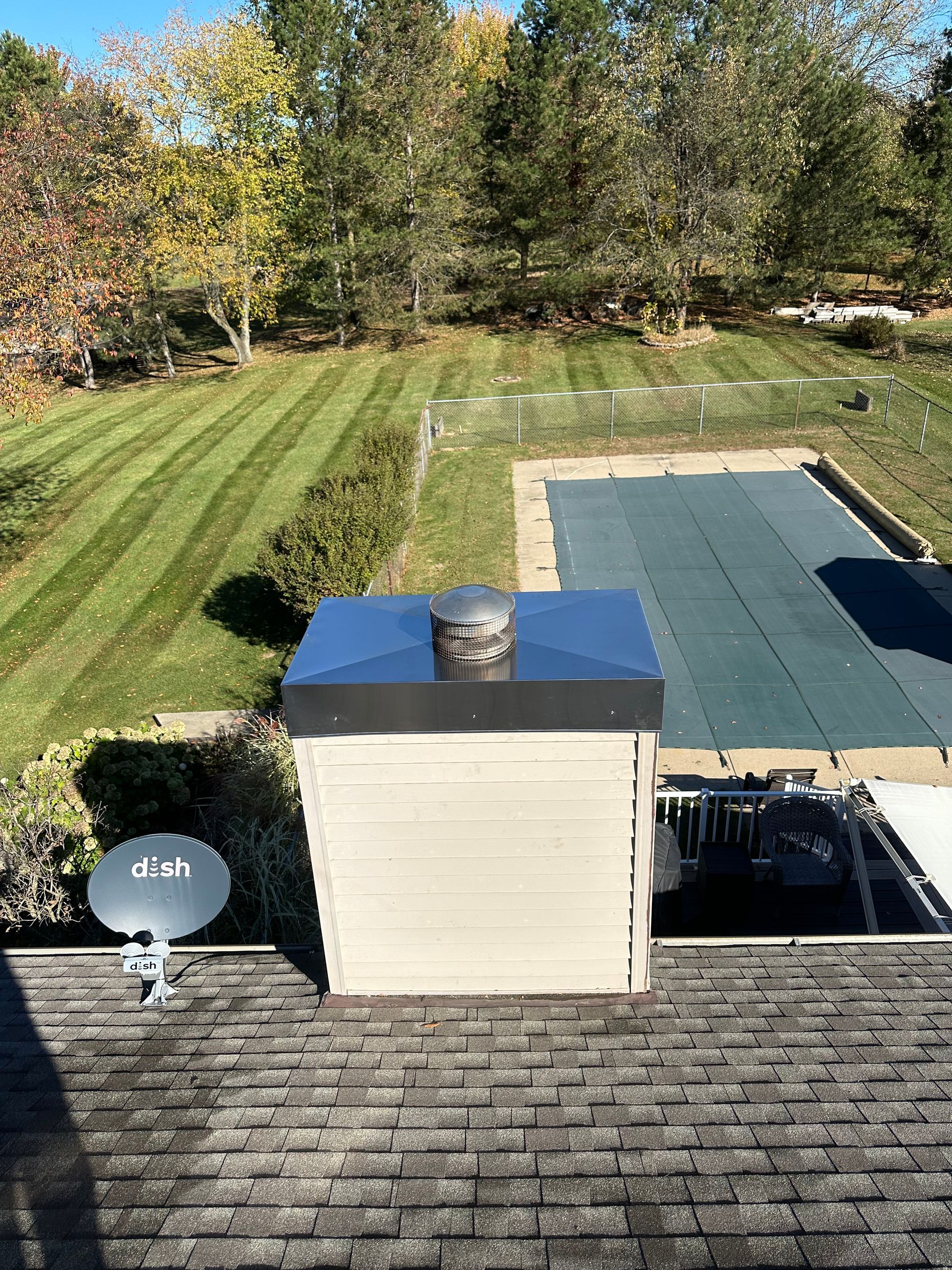 A brick chimney topped with a black wire mesh cap set against a clear blue sky.