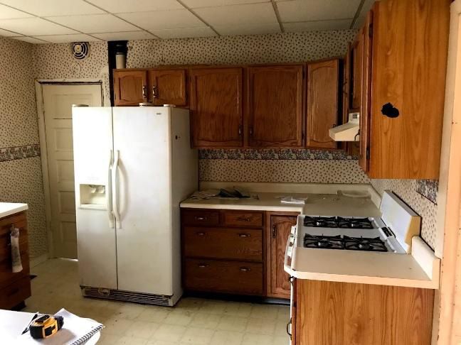 Kitchen with refrigerator, cabinets, and stove; floral wallpaper and linoleum floor.