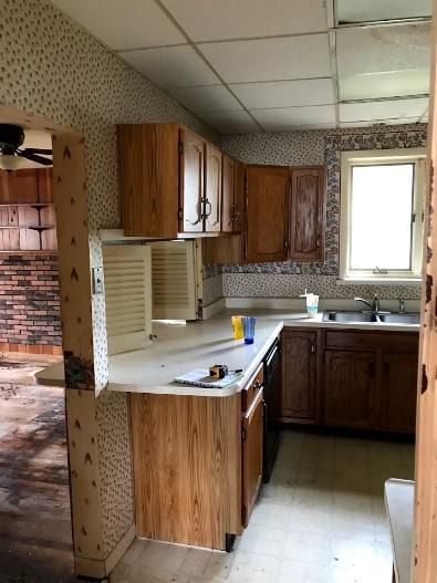 Kitchen with light wood cabinets, white countertops, and patterned wallpaper.