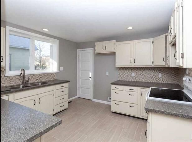 Kitchen with light-colored cabinets, gray countertops, and tile backsplash. Includes a window, door, and light-colored flooring.