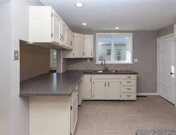 Cream-colored kitchen cabinets with gray countertops. Kitchen has tile floors and a window.