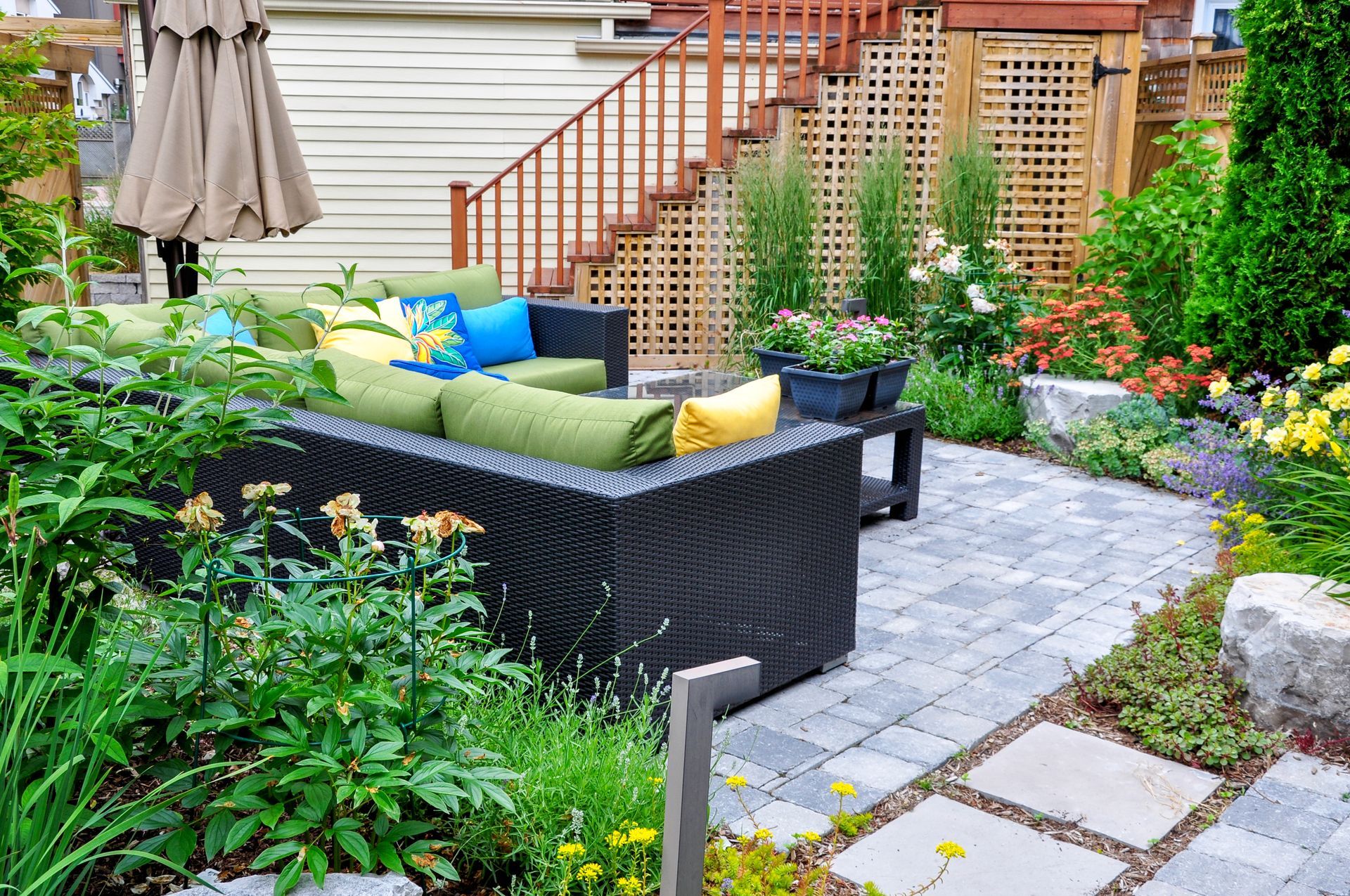 Backyard patio with wicker sofa, potted flowers, stone path, and wooden steps to a deck