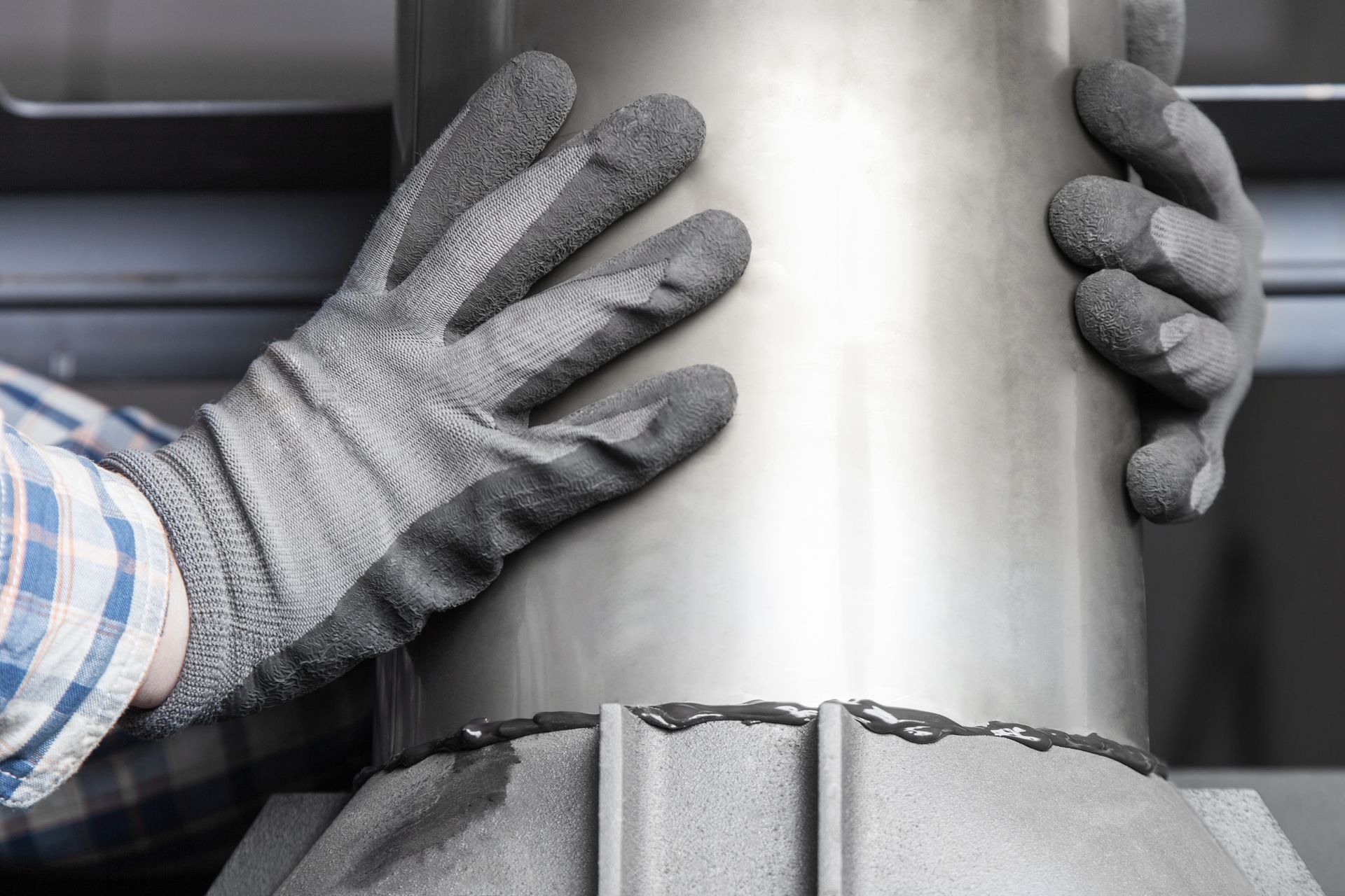 A person in gray work gloves grips a stainless steel chimney pipe mounted on a roof with visible sealant.