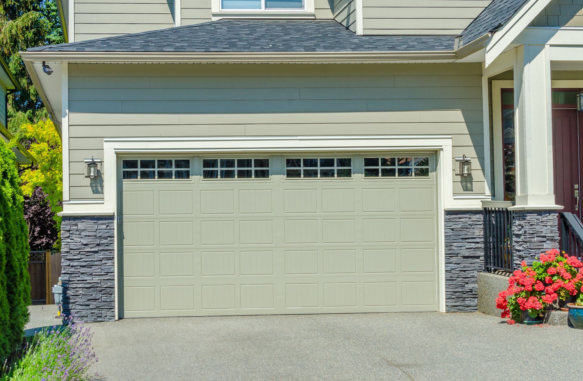 Light green residential garage door with a row of small rectangular windows, framed by stone siding and a paved driveway.