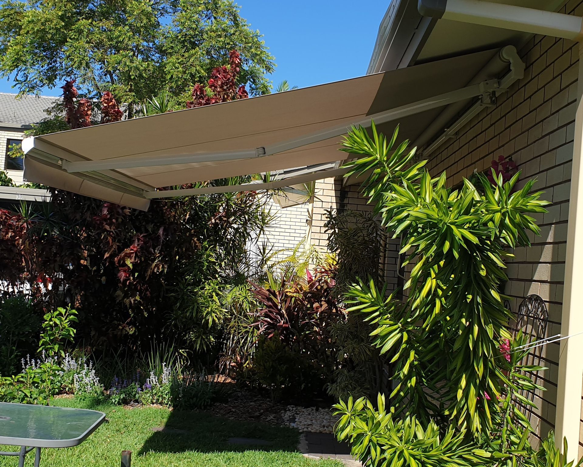 A Folding Arm Awning In A Garden Surrounded By Plants — Tropical Shade Blinds in Brinsmead, QLD