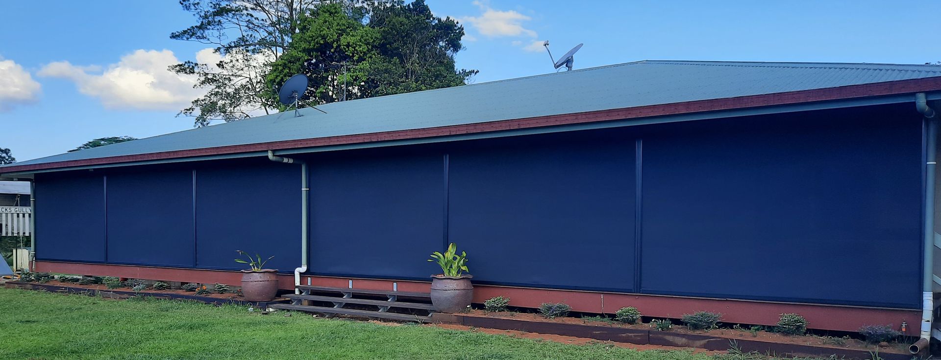 A Zip Screen With A Plant In Front With Some Brown Steps — Tropical Shade Blinds in Brinsmead, QLD