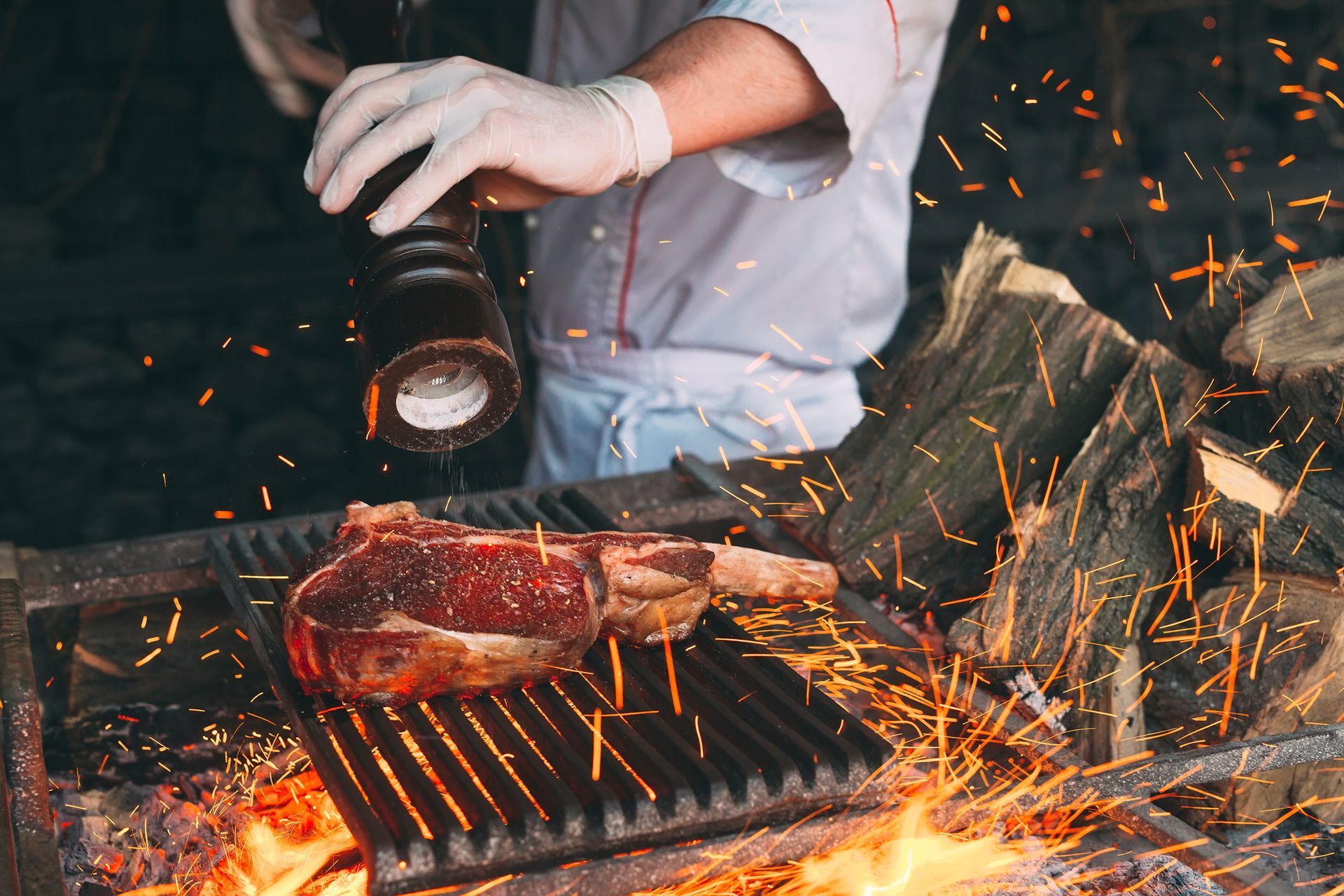 Chef seasoning a steak on a grill over a fire. Sparks fly.