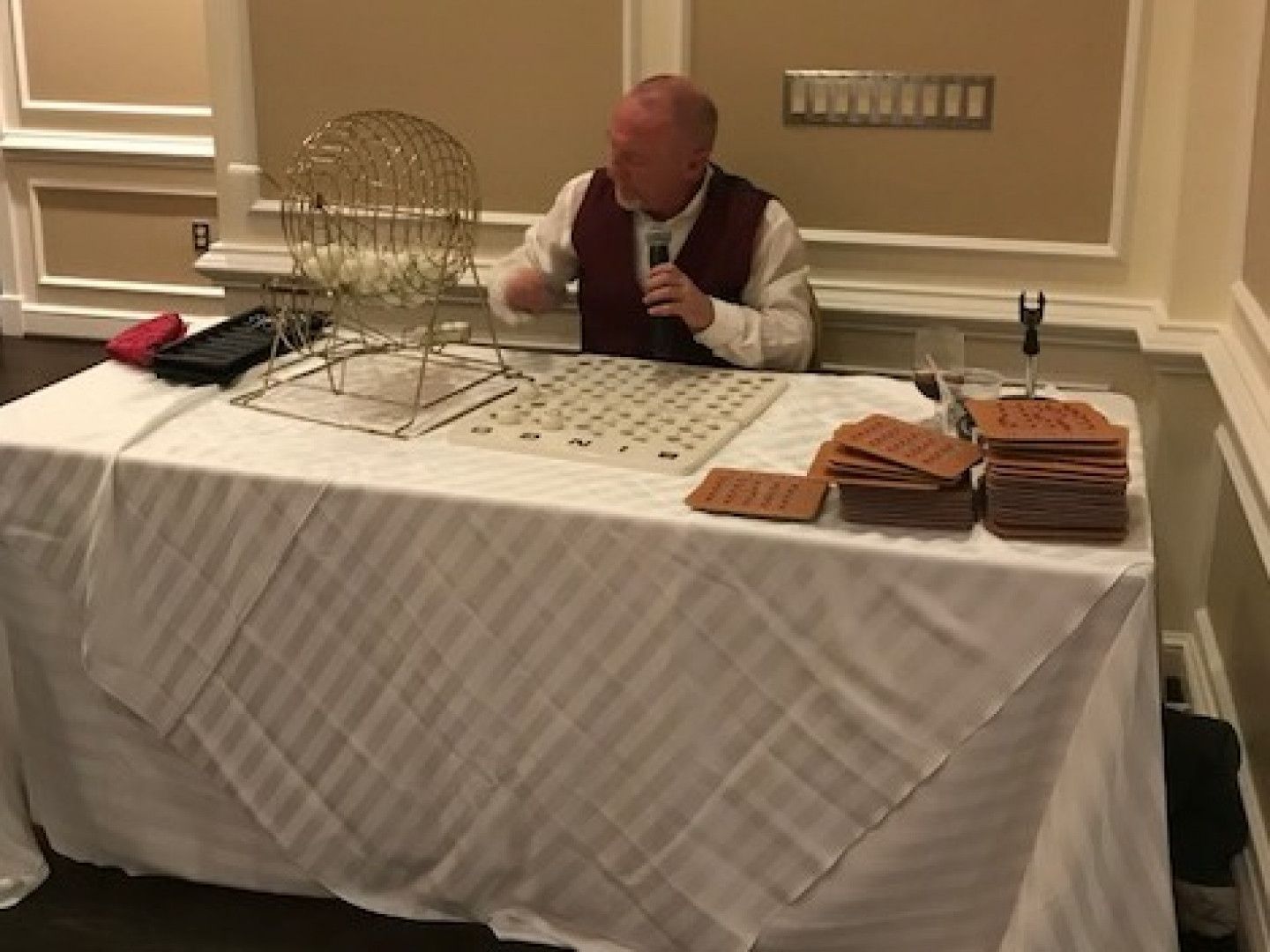 A man is sitting at a table with a microphone and a bingo cage.