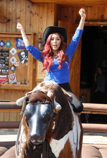 A woman is riding a bull with her arms in the air
