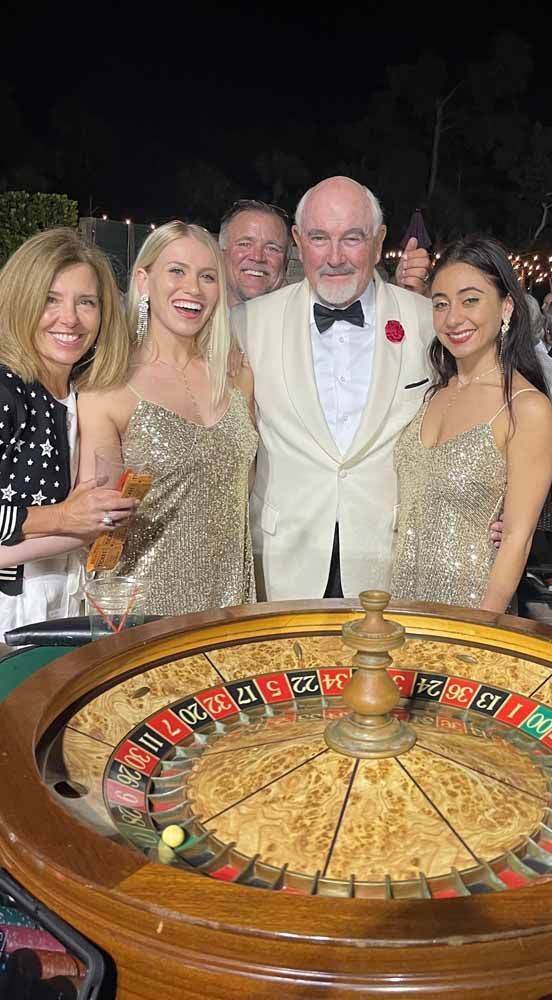 A group of people are posing for a picture in front of a roulette wheel.