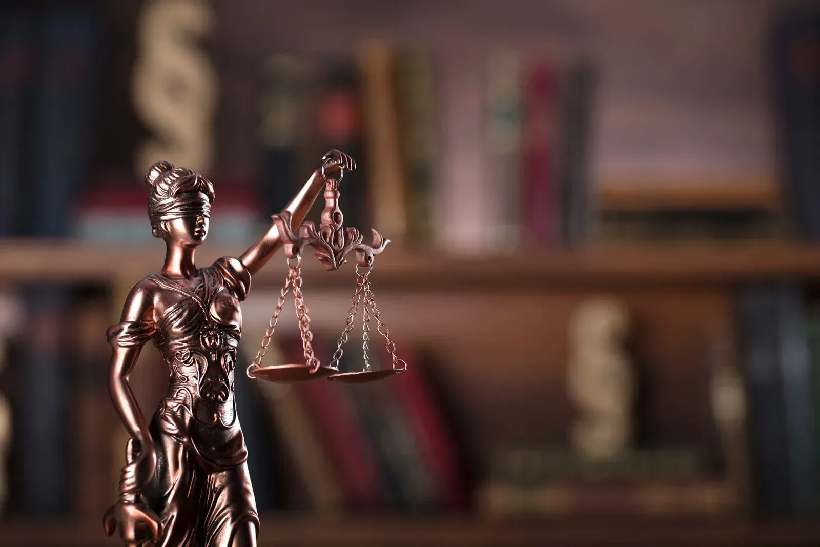 A statue of justice holding a scale in front of a bookshelf.