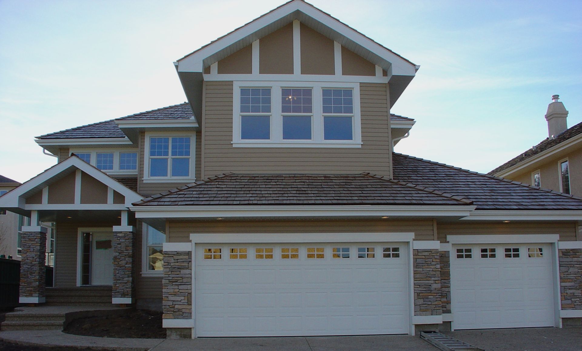 Two-story beige house with white trim, two garage doors, and stone accents.