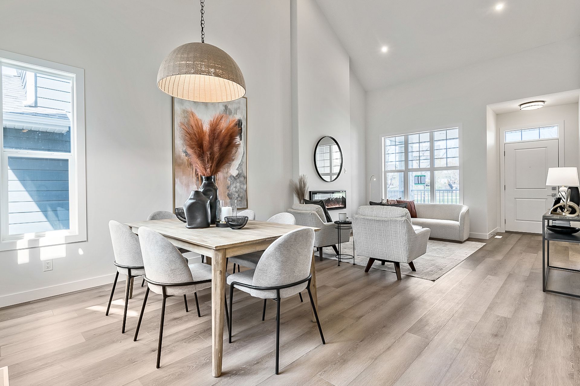 Bright dining room with wooden floors, table, chairs, and large artwork; living area in background.