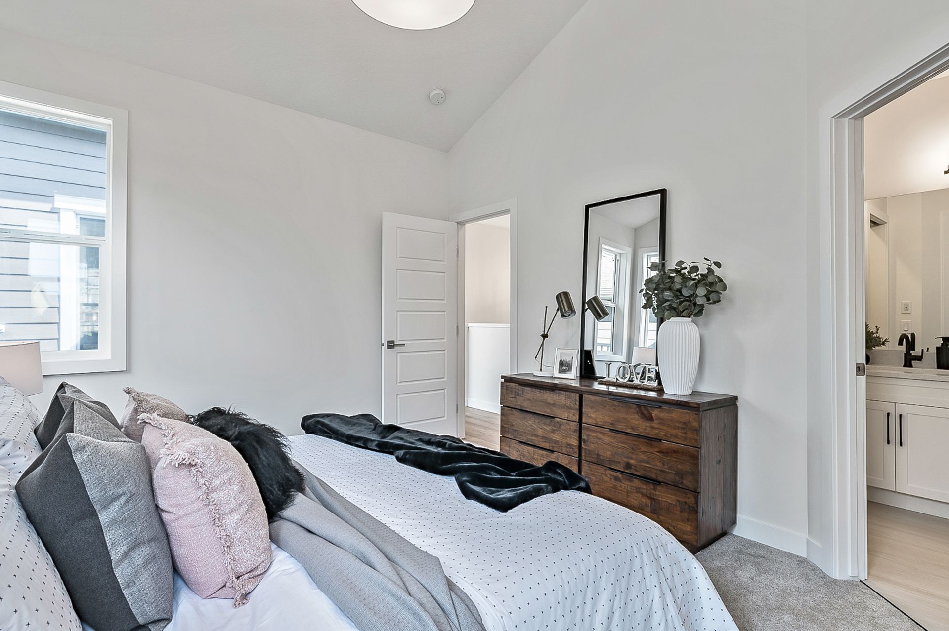 Bedroom with a bed, dresser, mirror, and doorway to a bathroom; white walls, neutral colors.