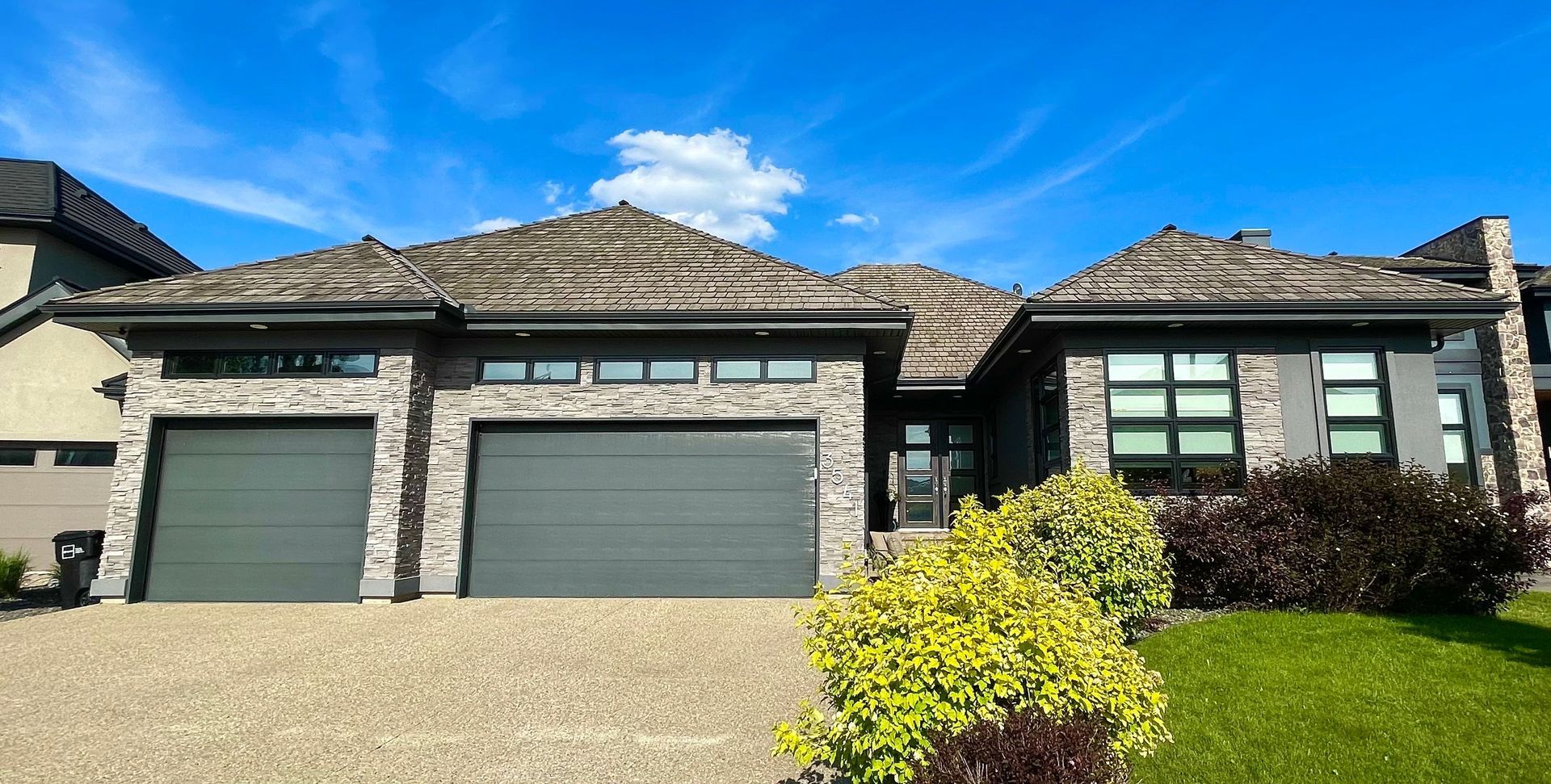 Modern house with stone facade, two-car garage, green door, and cedar shake roof, under blue sky.