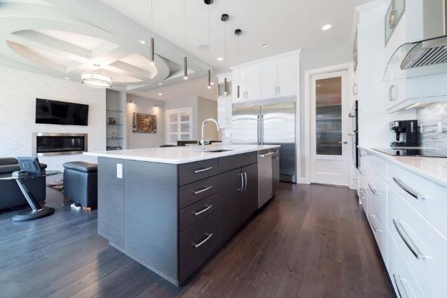 Modern kitchen with gray island, white cabinets, and dark wood floors.