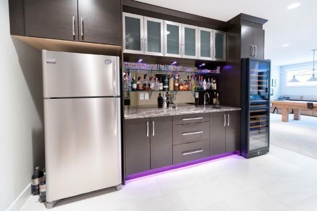 Home bar with a fridge, wine cooler, cabinets, and liquor bottles.