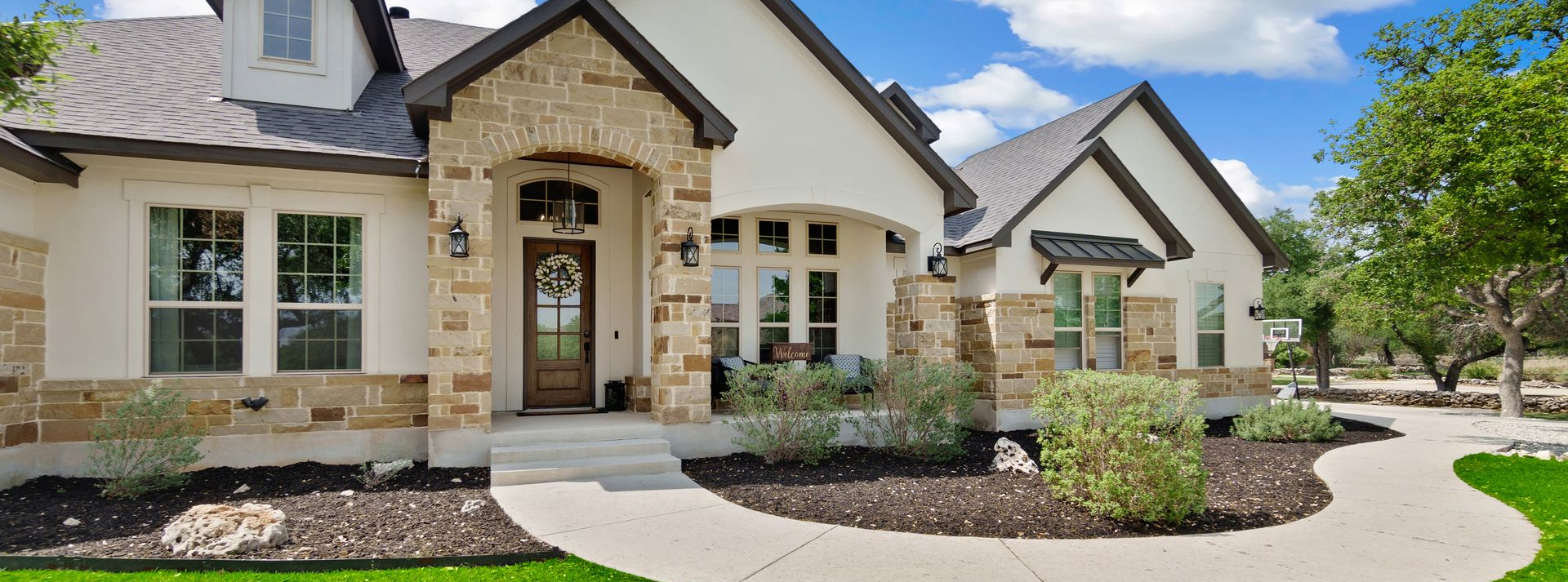 Exterior view of a house with a stone arch entryway, white walls, and a paved walkway leading to a front door.