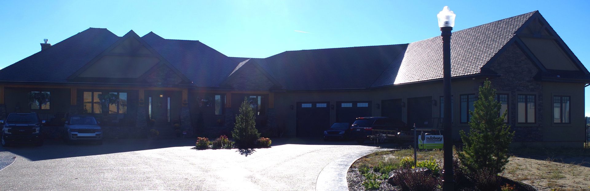 A large, dark-colored house with a winding driveway on a sunny day.