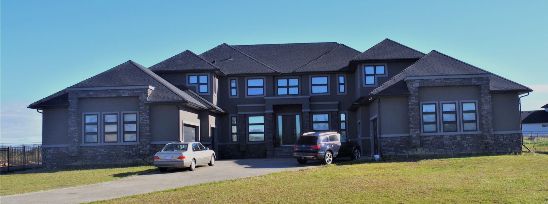 Large gray house with two cars in front on a sunny day.