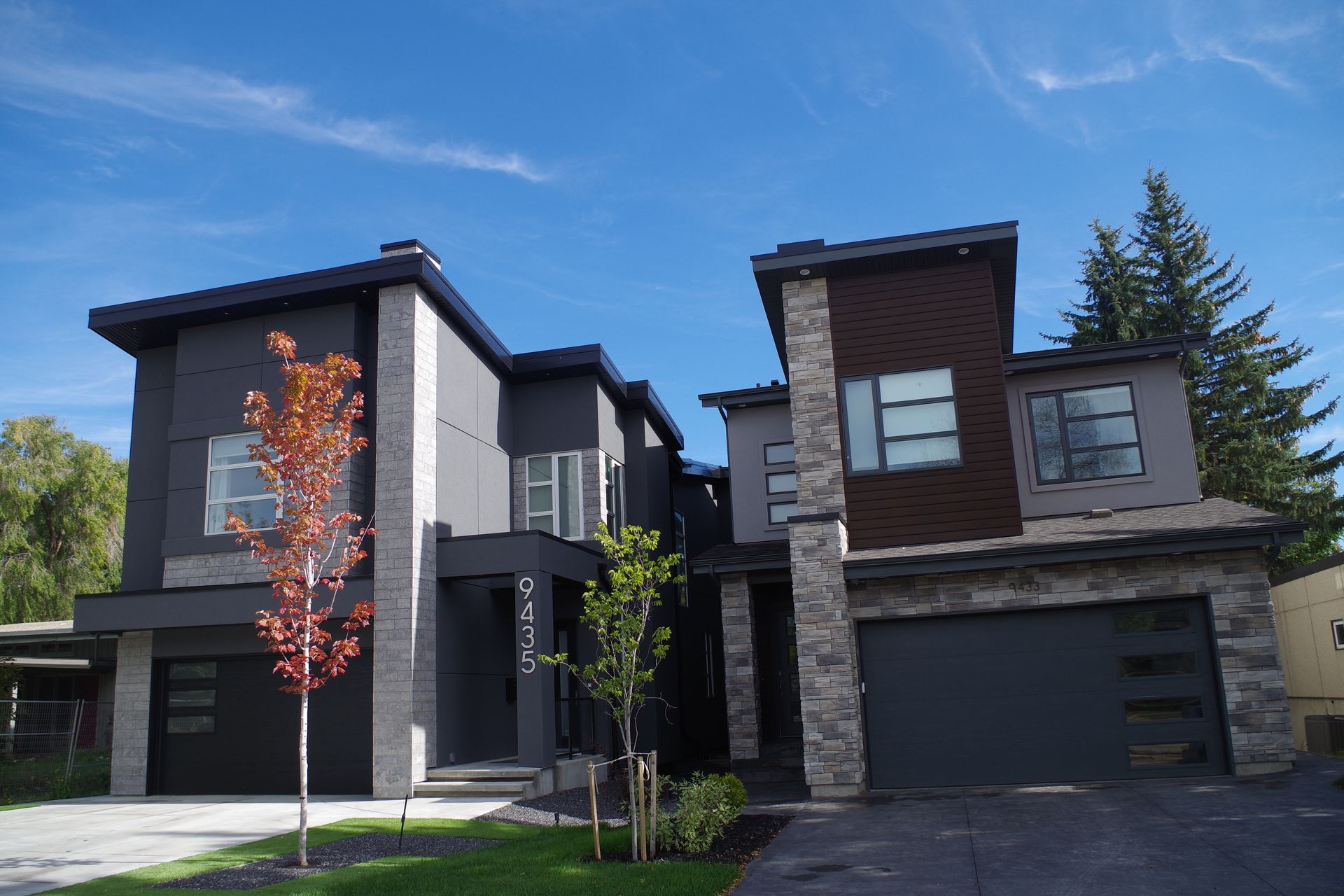 Two modern houses with dark gray siding, stone accents, and a blue sky.