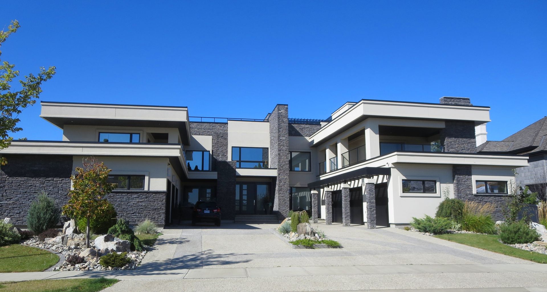 Modern two-story house with gray stone, black accents, and a blue sky.