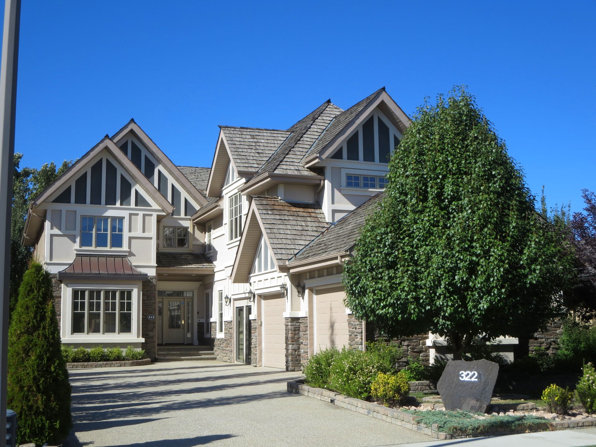 Two-story house with light stucco, stone accents, and a gray roof on a bright day.